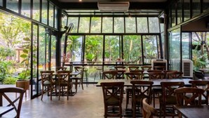 An indoor dining area with large windows, wooden tables and chairs, and an air conditioning unit. - Crystal Resort (Nakhon Ratchasima)