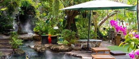 A serene outdoor pool area with a waterfall, wooden deck, and lounge chairs.