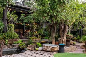 A lush garden with a wooden deck, a pond, and various plants. - Crystal Resort (Nakhon Ratchasima)