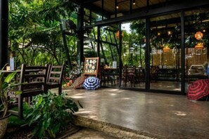 An indoor space with tables and chairs, surrounded by glass walls and potted plants. - Crystal Resort (Nakhon Ratchasima)