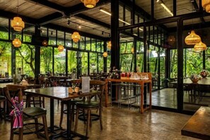 An indoor dining area with tables and chairs, large windows, and hanging pendant lights. - Crystal Resort (Nakhon Ratchasima)