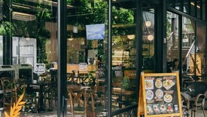 A restaurant with a menu board outside, indoor seating, and greenery visible through the windows. - Crystal Resort (Nakhon Ratchasima)
