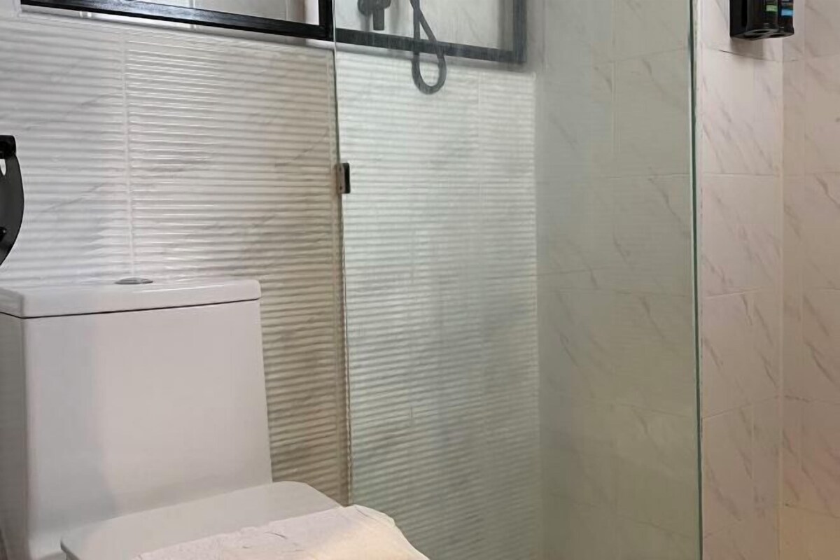 Ein Badezimmer mit Toilette, einer Duschkabine aus Glas und einer gefliesten Wand.
