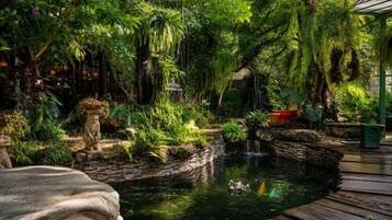 A lush garden with a pond, wooden deck, and various plants.