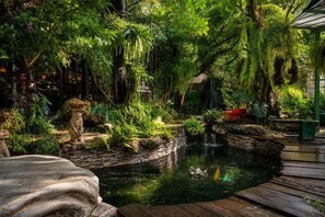 A lush garden with a pond, wooden deck, and various plants. - Crystal Resort (Nakhon Ratchasima)