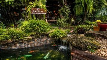 Un jardin intérieur luxuriant avec un bassin, une cascade et une enseigne indiquant « CRYSTAL CAFÉ, DESSERTS ET ENCAS ».
