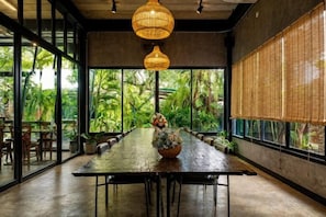 A long dining table with chairs, a vase with flowers, and hanging wicker lamps. - Crystal Resort (Nakhon Ratchasima)