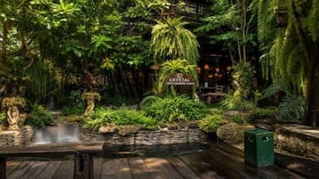 Un jardin intérieur luxuriant, agrémenté d’une cascade, de bancs en pierre et d’une pancarte sur laquelle on peut lire « CRYSTAL ».