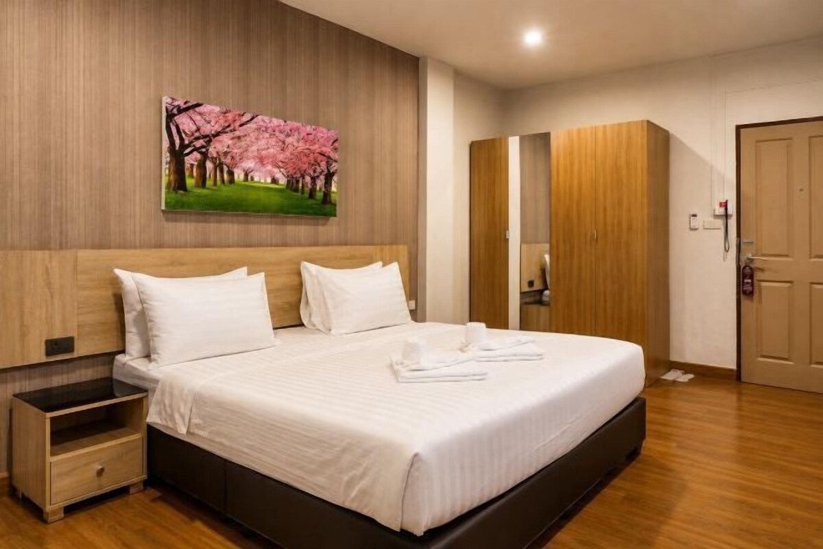 Habitació d'hotel amb un llit gran, un panell de fusta al capçal, una tauleta de nit, un armari i un quadre a la paret.