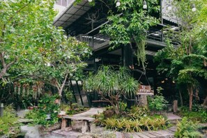 A lush garden with a wooden bench, a small pond, and a sign indicating a restaurant. - Crystal Resort (Nakhon Ratchasima)