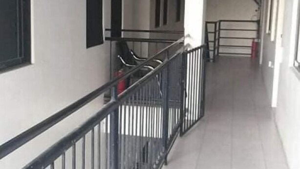 A corridor with a metal railing, tiled floor, and a staircase leading to an upper level.