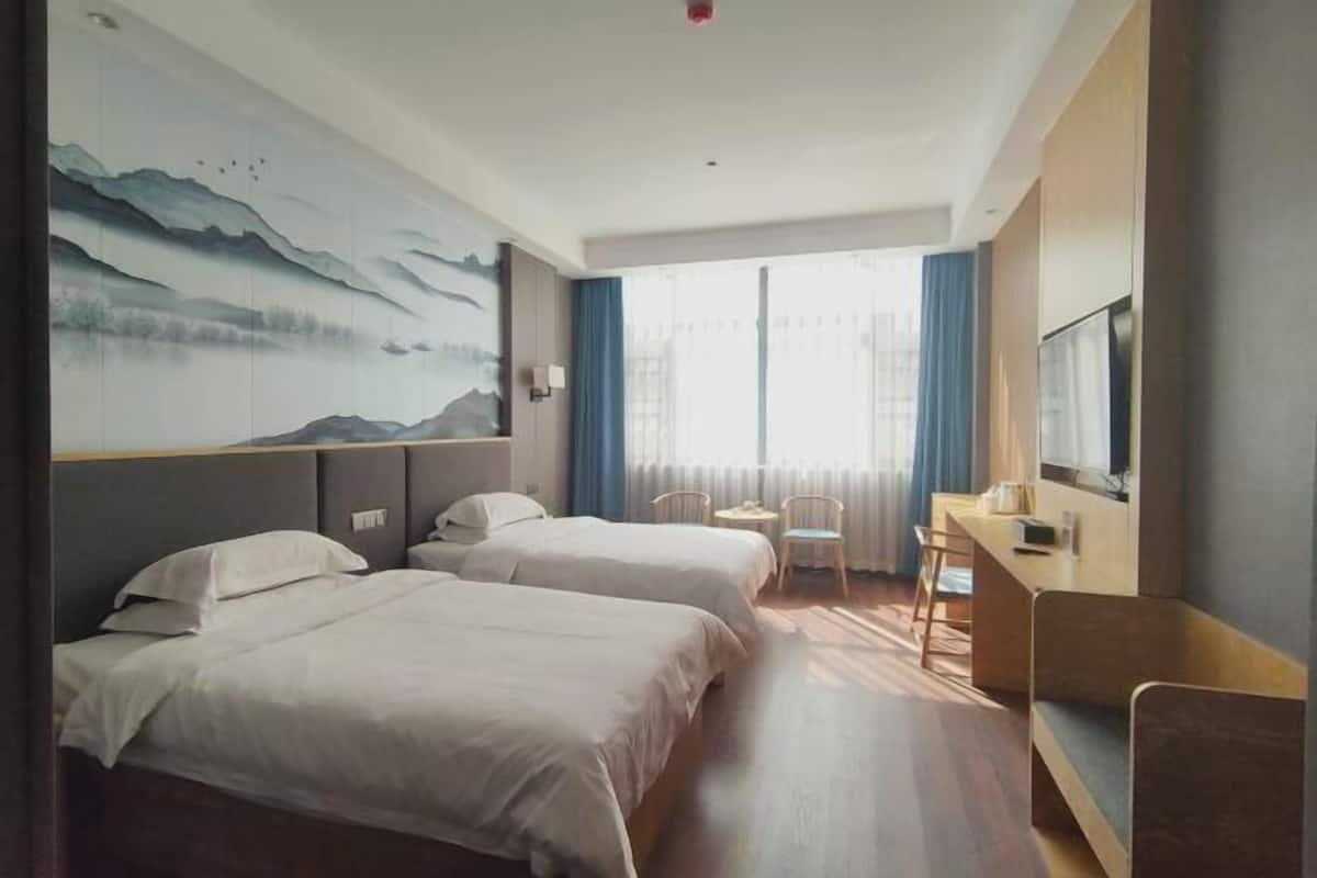 A hotel room with two beds, a desk, a chair, and a large window with curtains.