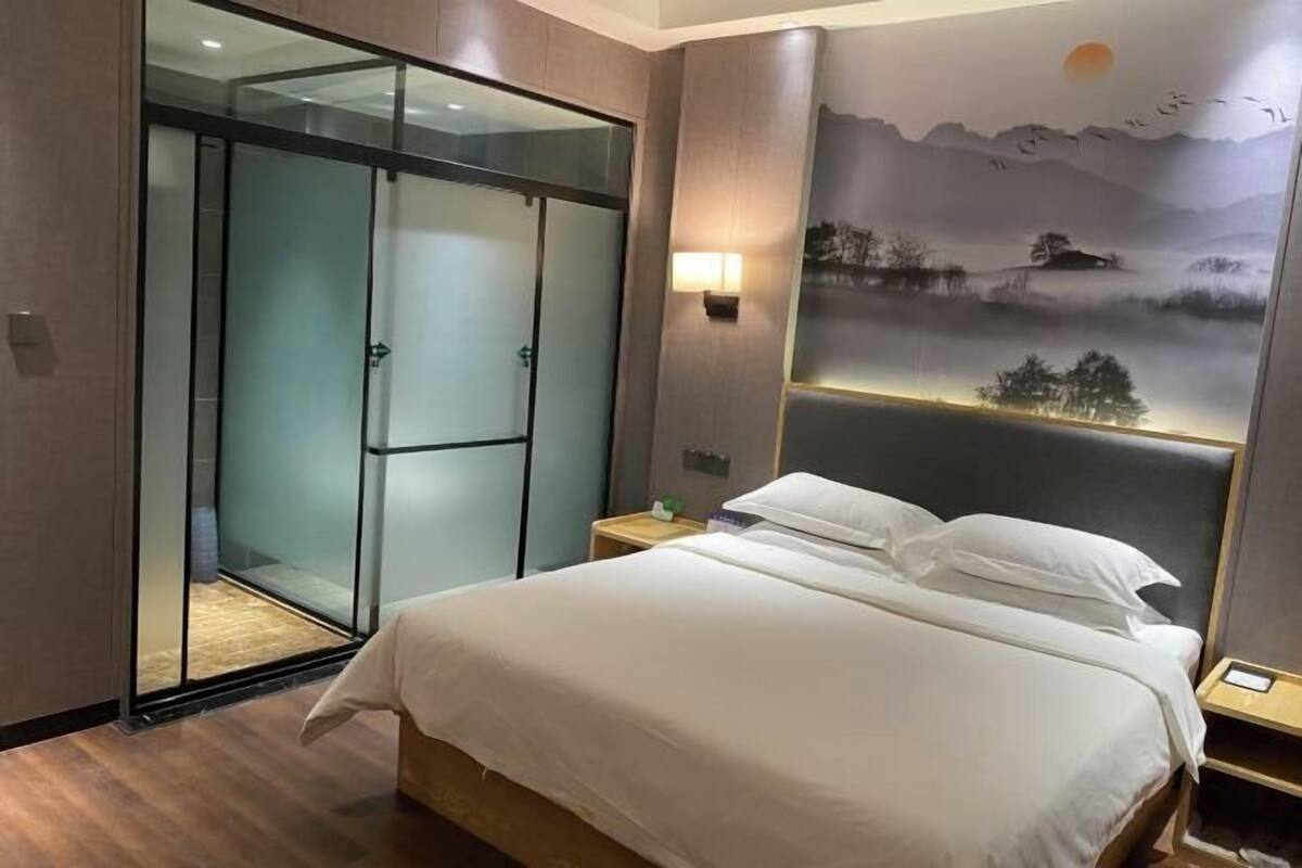 A hotel room with a bed, a glass door closet, and a wall-mounted light fixture.