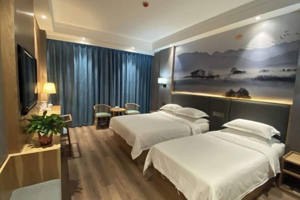 A hotel room with two beds, a desk with a chair, a TV, and a wall with a scenic mural.