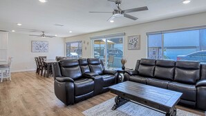 A spacious living room with leather sofas, a dining area, and a large window offering a view of the street. - Monthly Only - Remodeled Lower Unit Just One House To The Sand With AC (Newport Beach)