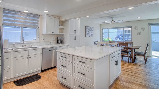 A modern kitchen with white cabinetry, a large island, and a dining area with wooden chairs and a table. - Monthly Only - Remodeled Lower Unit Just One House To The Sand With AC (Newport Beach)
