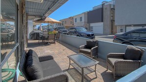 An outdoor patio with wicker furniture, a glass table, and an umbrella. - Monthly Only - Remodeled Lower Unit Just One House To The Sand With AC (Newport Beach)