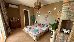 Une chambre avec un lit, une cheminée en briques et une grande fenêtre.