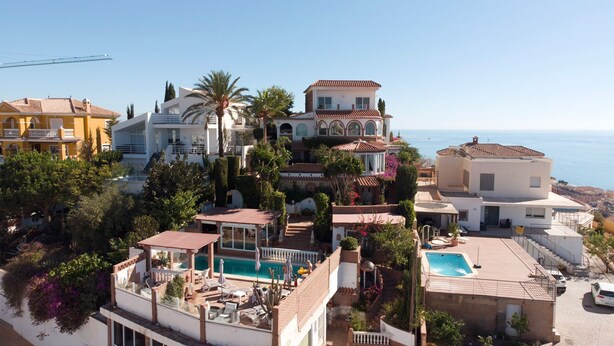 Un quartier résidentiel situé sur la côte, composé de plusieurs bâtiments, dont une grande maison avec une piscine et un bâtiment plus petit doté d’un jacuzzi.