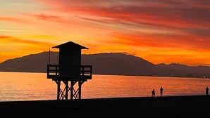 Une tour de surveillance où se tient un sauveteur, surplombant une étendue d’eau avec des montagnes en arrière-plan.