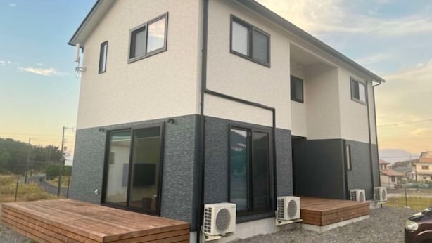 Una casa moderna de dos pisos con techo plano, ventanas amplias y terraza de madera.