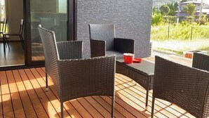 Un patio con mobiliario de mimbre y una taza roja sobre una terraza de madera.