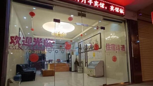 A hotel entrance with a reception desk, a chandelier, and a red welcome mat.