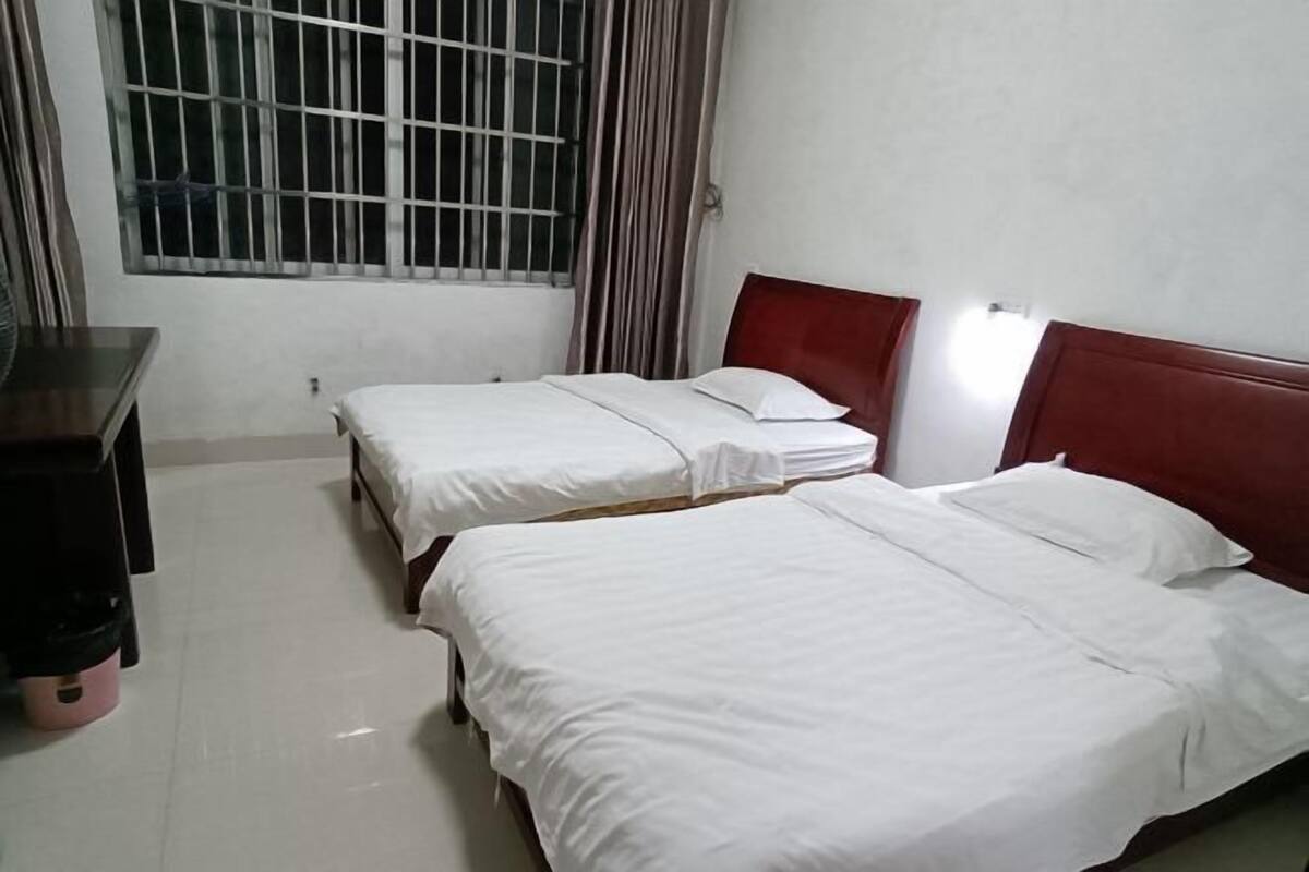 A hotel room with two single beds, a wooden dresser, a window with bars, and a curtain.
