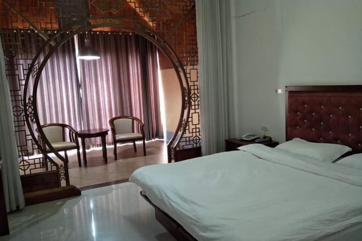A hotel room with a bed, a chair, a small table, a phone, and a curtain.