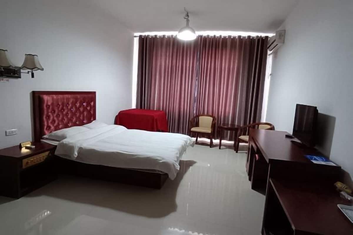 A hotel room with a bed, a desk, a chair, a television, and a window with curtains.