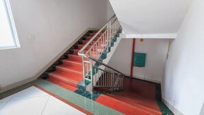 A staircase with red steps and a metal railing, leading to a landing with a green wall and a white ceiling.