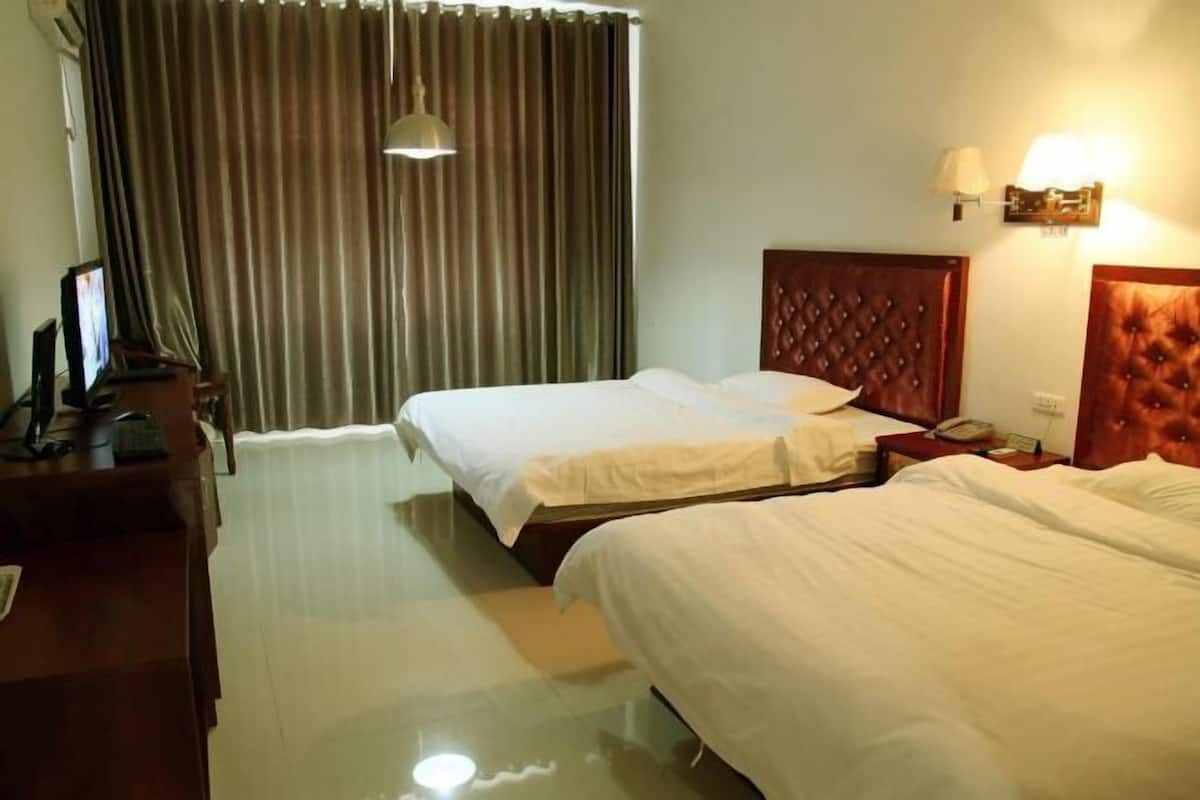 A hotel room with two beds, a desk, a chair, a lamp, and a curtain.