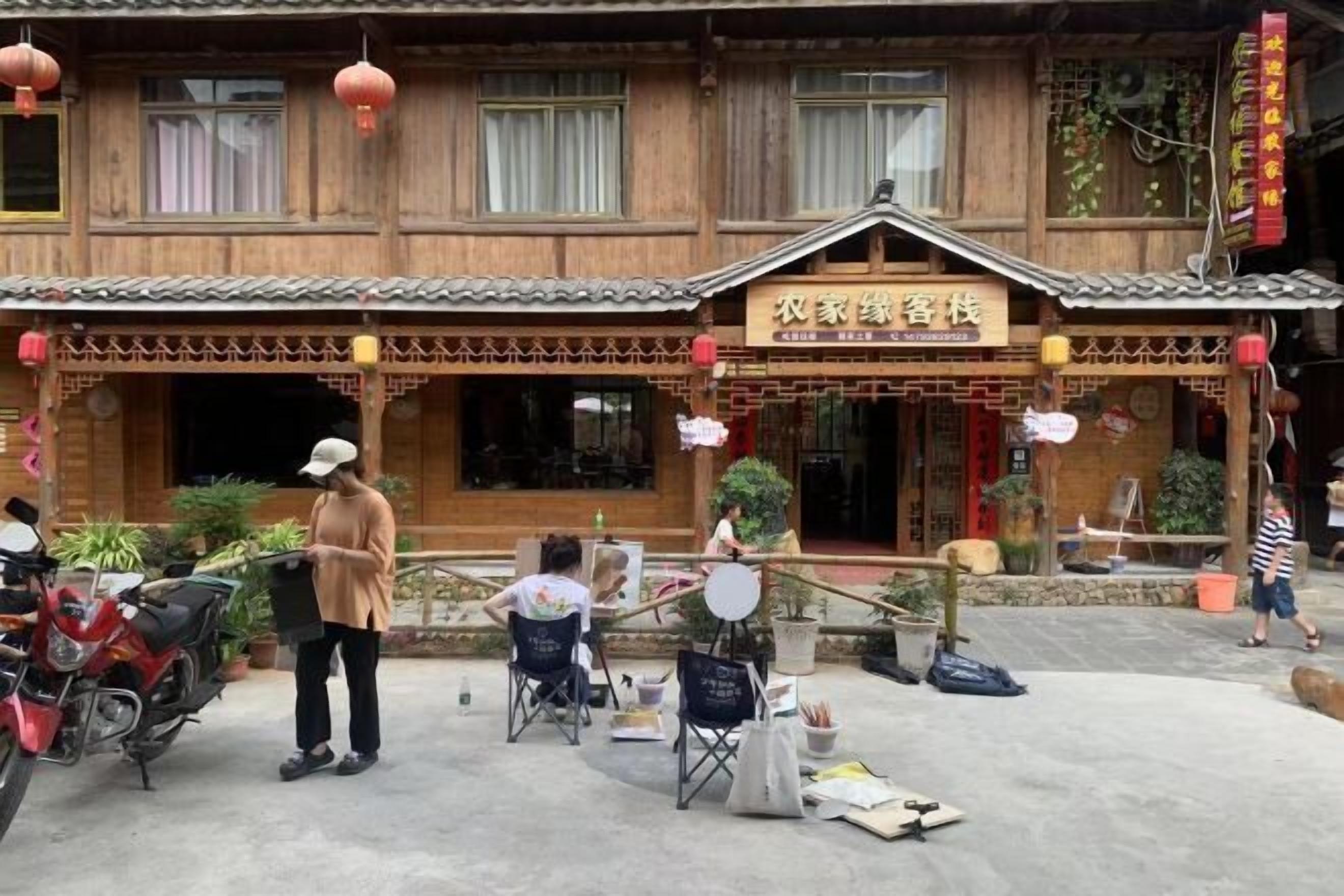 A traditional wooden building with a sign indicating a guesthouse. There are outdoor seating areas with tables and chairs, and a motorcycle parked outside.