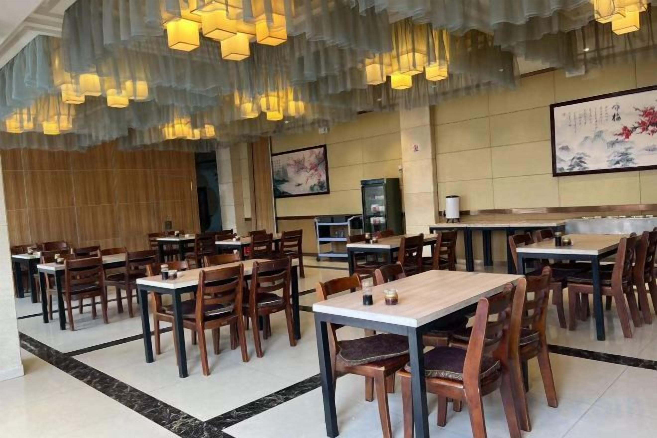 Un restaurante con varias mesas y sillas, piso de madera y lámparas colgantes.