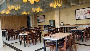 Un restaurante con varias mesas y sillas, piso de madera y lámparas colgantes.
