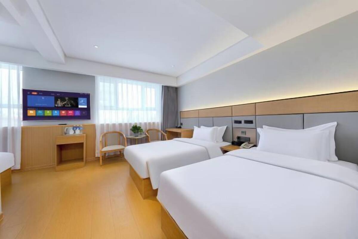 A hotel room with two beds, a desk, a chair, a TV, and a window.