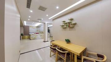 A modern dining area with a wooden table and chairs, a reception desk in the background, and a clean, well-lit interior.
