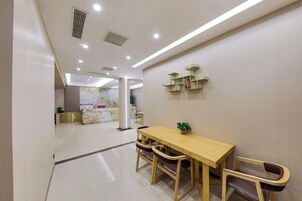 A modern dining area with a wooden table and chairs, a reception desk in the background, and a clean, well-lit interior.