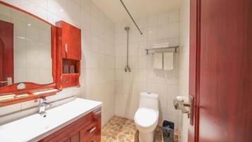Un baño con un lavabo blanco, tocador de madera, un armario rojo, inodoro blanco, ducha y suelo de baldosas.