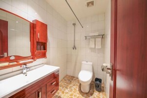 Un baño con un lavabo blanco, tocador de madera, un armario rojo, inodoro blanco, ducha y suelo de baldosas.