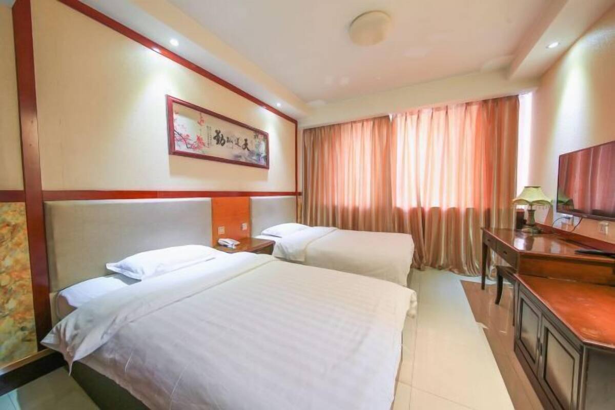 A hotel room with two beds, a desk, a television, and a framed artwork on the wall.