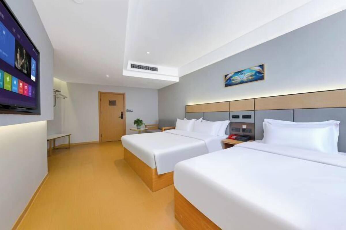 A hotel room with two beds, a TV, a painting, and a door.