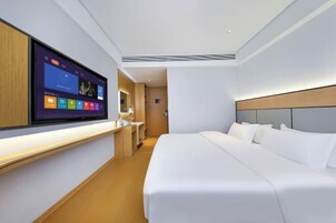 Una habitación de hotel moderna con un televisor de pantalla plana grande montado en la pared, una cama bien hecha y una mesita de noche de madera.