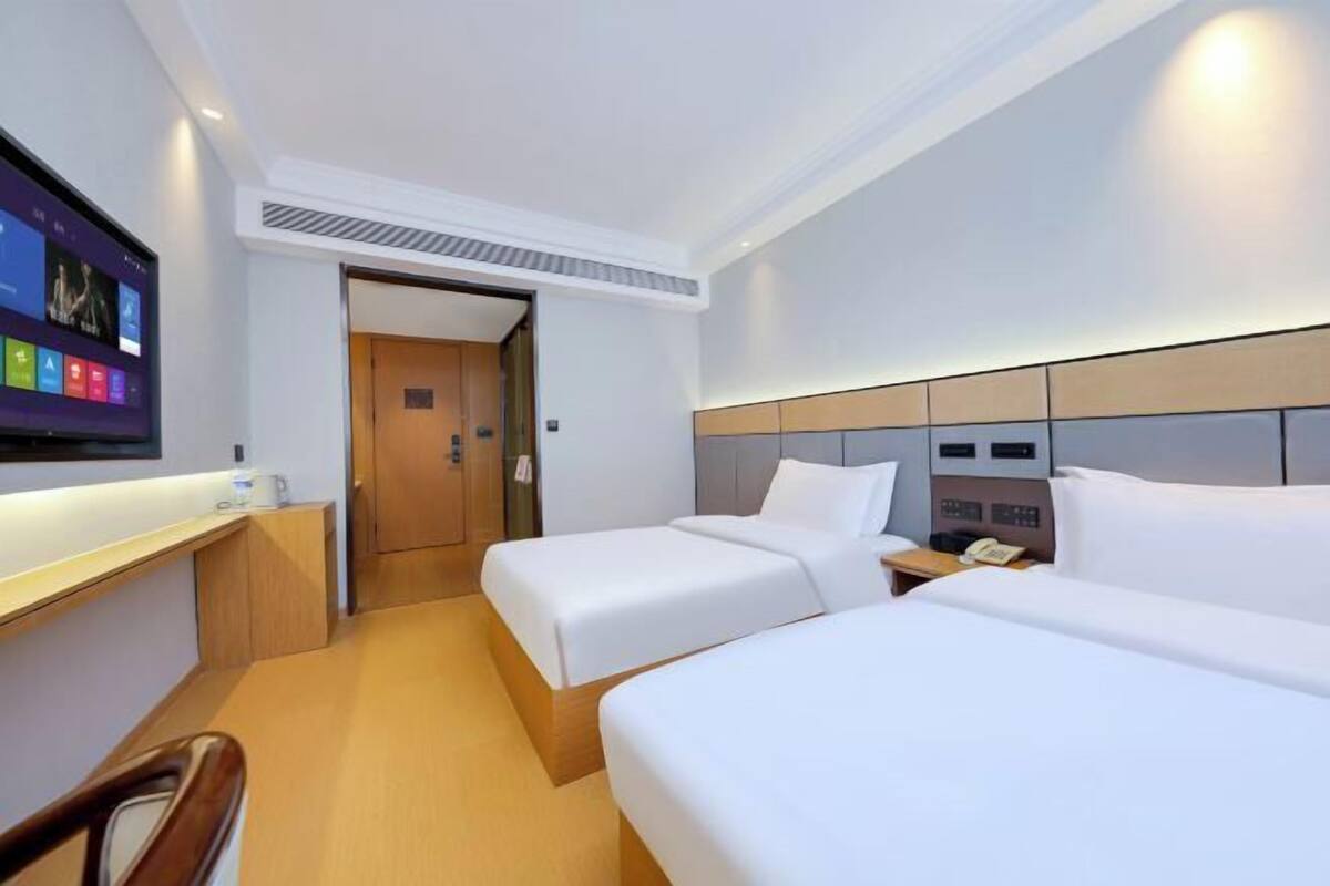 A hotel room with two beds, a desk, a TV, and a door leading to another room.