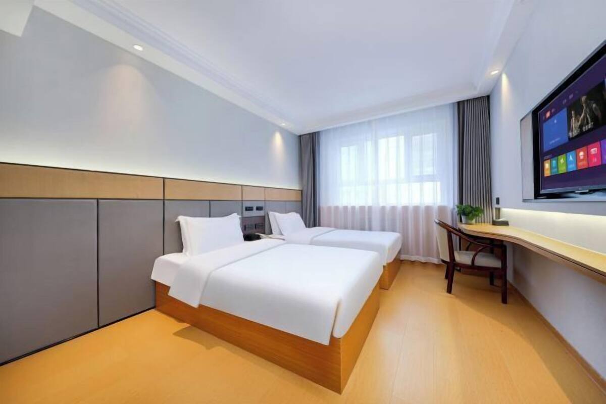 A hotel room with two beds, a desk, a TV, and a window with curtains.