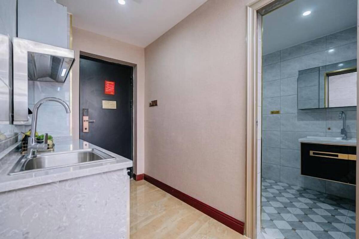 Une cuisine moderne avec un évier en acier inoxydable, une porte noire avec une enseigne rouge, et une salle de bain avec un carrelage à motifs et un miroir.