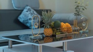 Une cuisine moderne avec un plan de travail en verre, un ananas, un panier d’oranges et une petite plante.