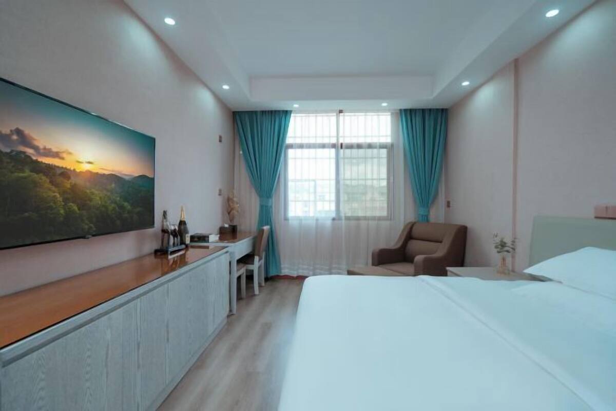 Une chambre d’hôtel avec un lit, un bureau, une chaise, une télévision et une fenêtre avec des rideaux.