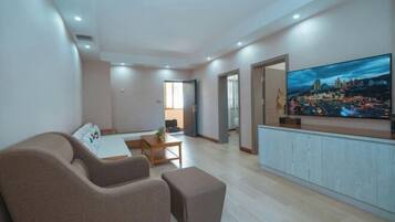 A modern living room with a flat-screen TV, a sofa, a coffee table, and a dining area.