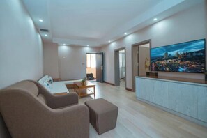 A modern living room with a flat-screen TV, a sofa, a coffee table, and a dining area.